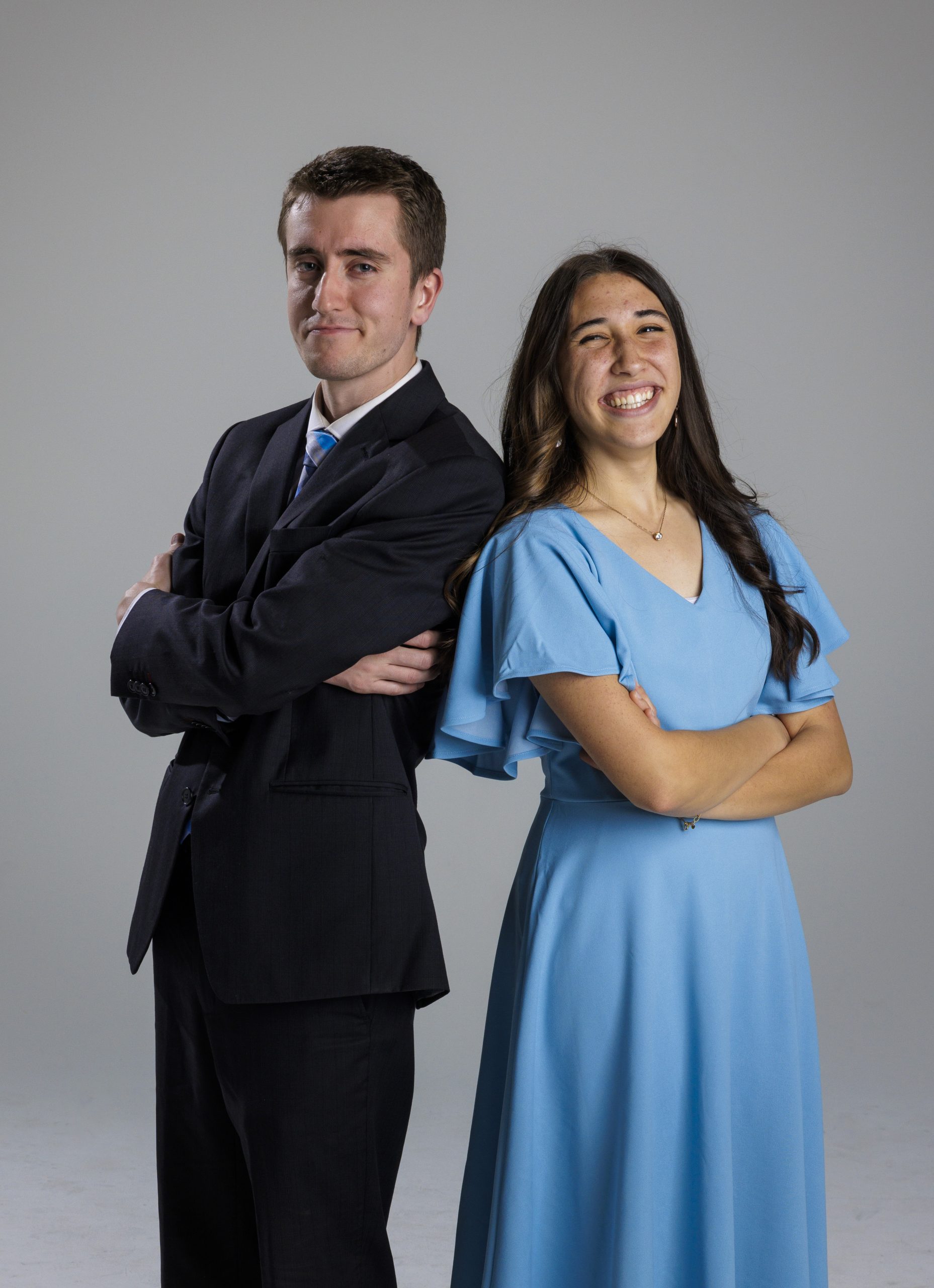 2 BYU Synthesis vocalists pose back to back in concert attire. They smile with their arms crossed.