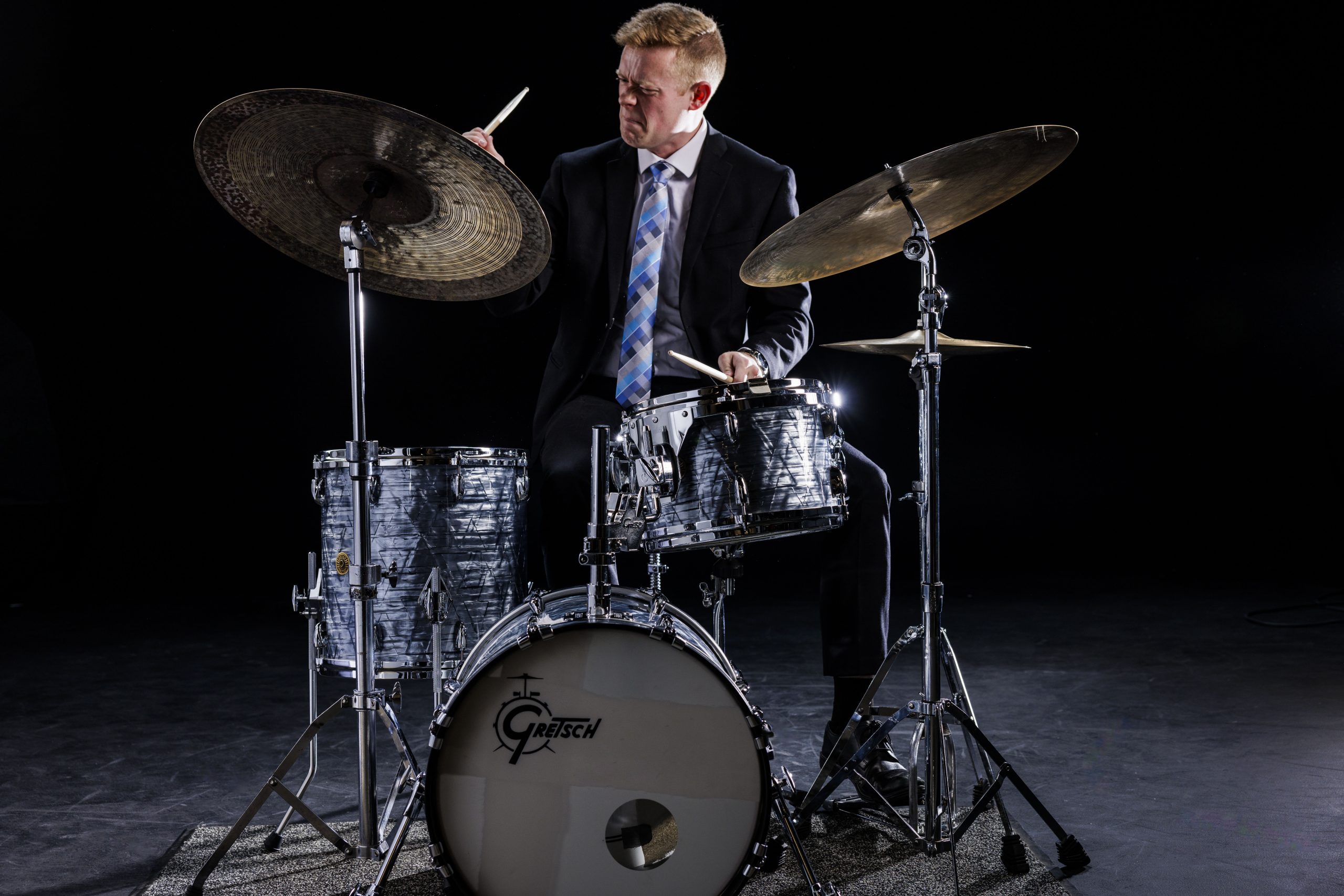 BYU Synthesis drummer plays a beat on his drum kit against a black studio backdrop in formal dress
