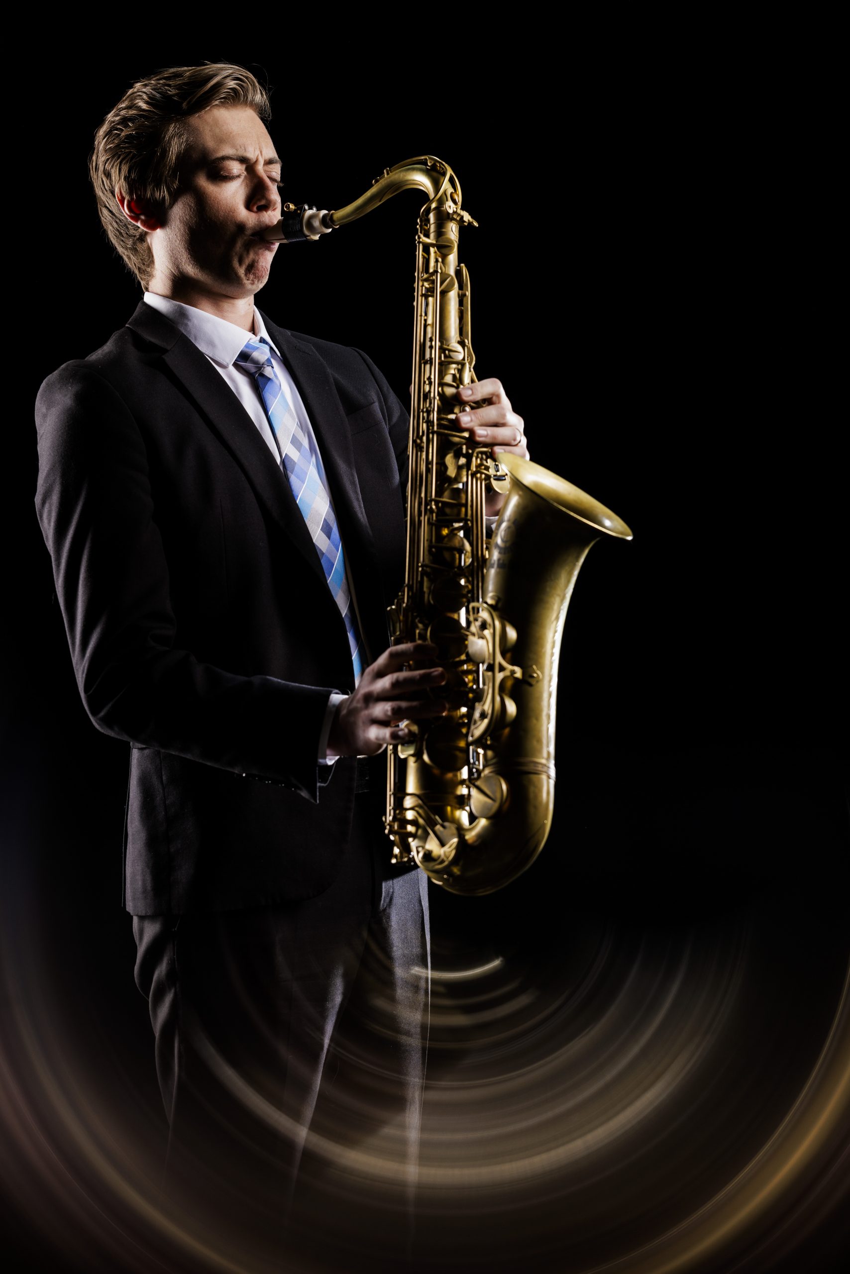 BU Synthesis saxophone player plays a solo against a black backdrop, wearing concert attire.