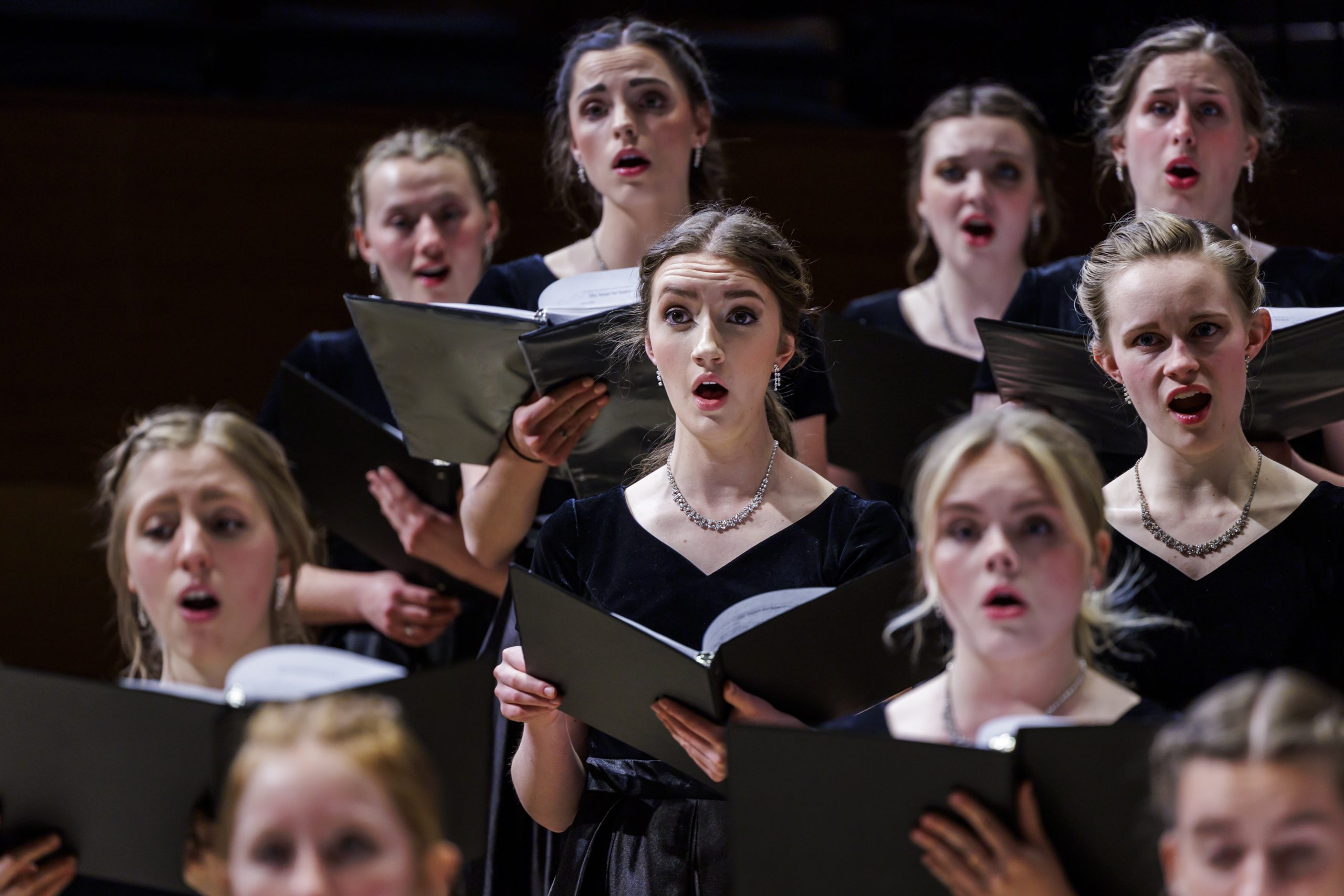 BYU Women's Chorus first soprano section, singing from black folders in concert black attire.