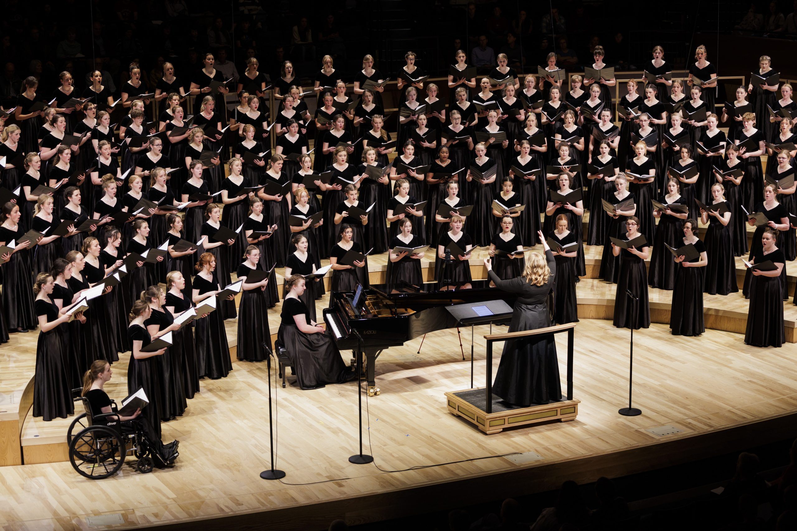 Brigham Young University Women’s Chorus performing on stage in formal black dresses, standing in riser formation under concert lighting.