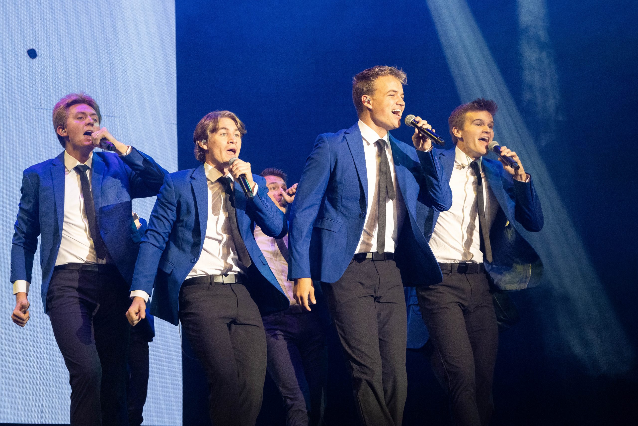 Vocal Point members sing at BYU-Idaho for Date Night in navy blue suits, holding microphones and performing choreography.
