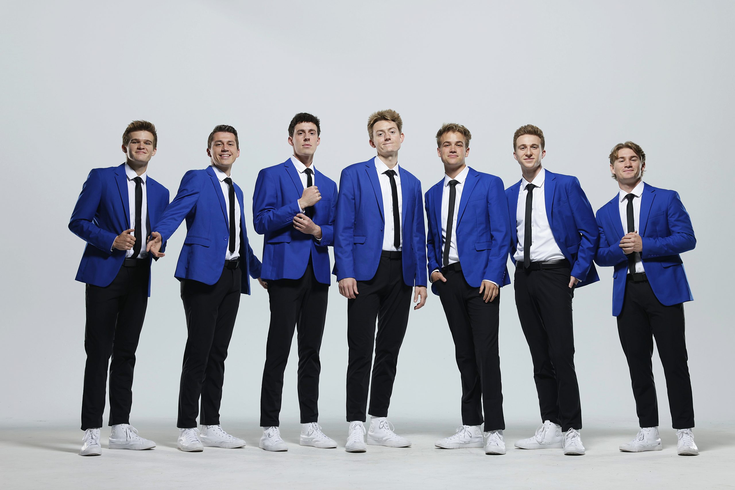 Vocal Point members smile together in their navy blue suits against a white backdrop