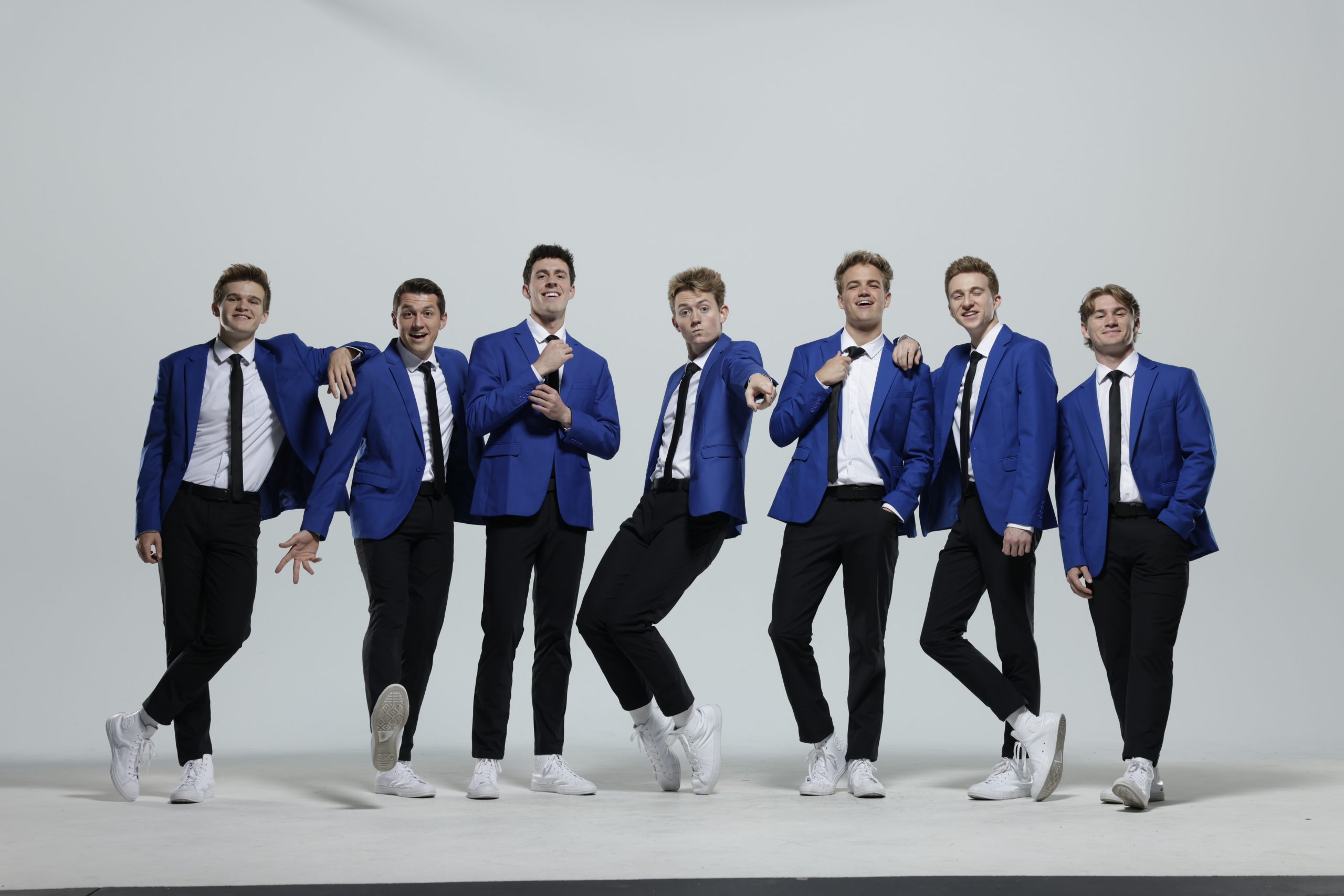 Vocal Point members pose in their navy blue suits against a white backdrop.